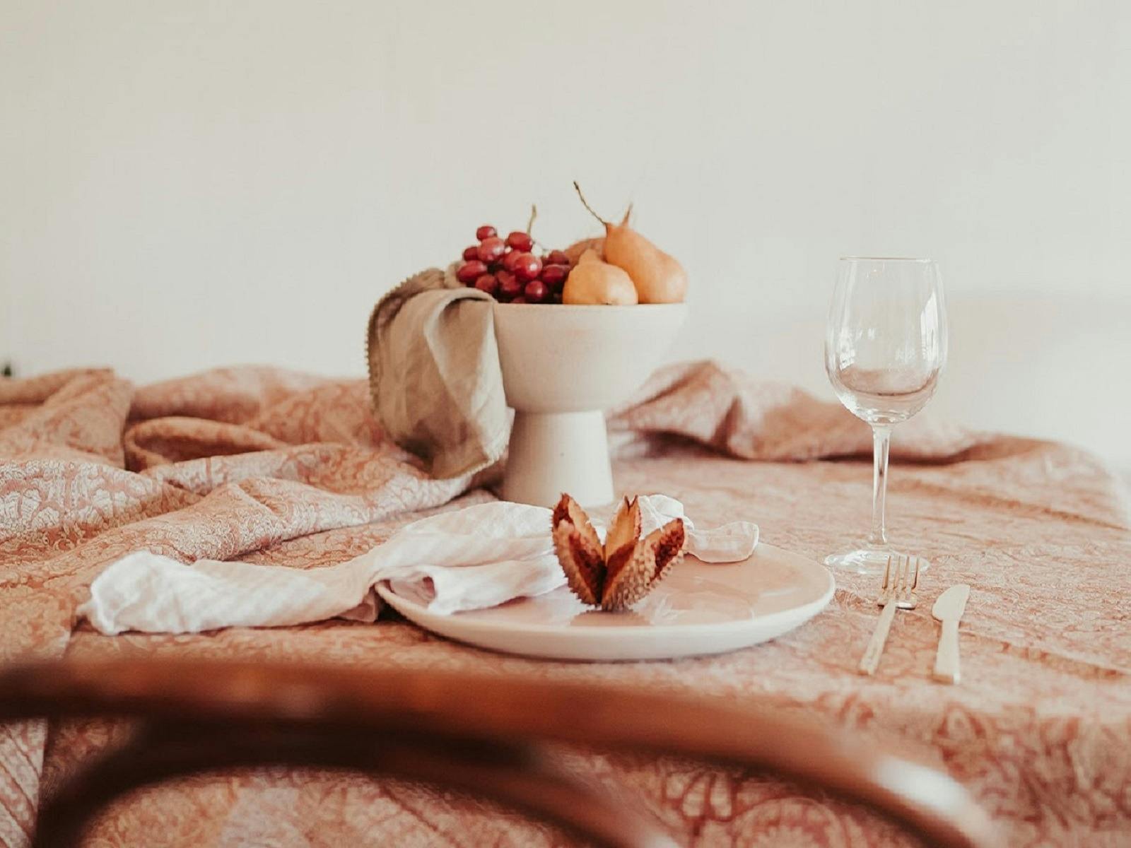 grapes and pears in a white bowl next to a plate, cutlery and a wine glass on a peach table cloth