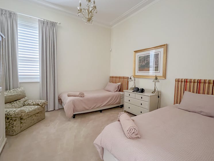 Large bedroom, vintage chair, two king single beds and a bedside table