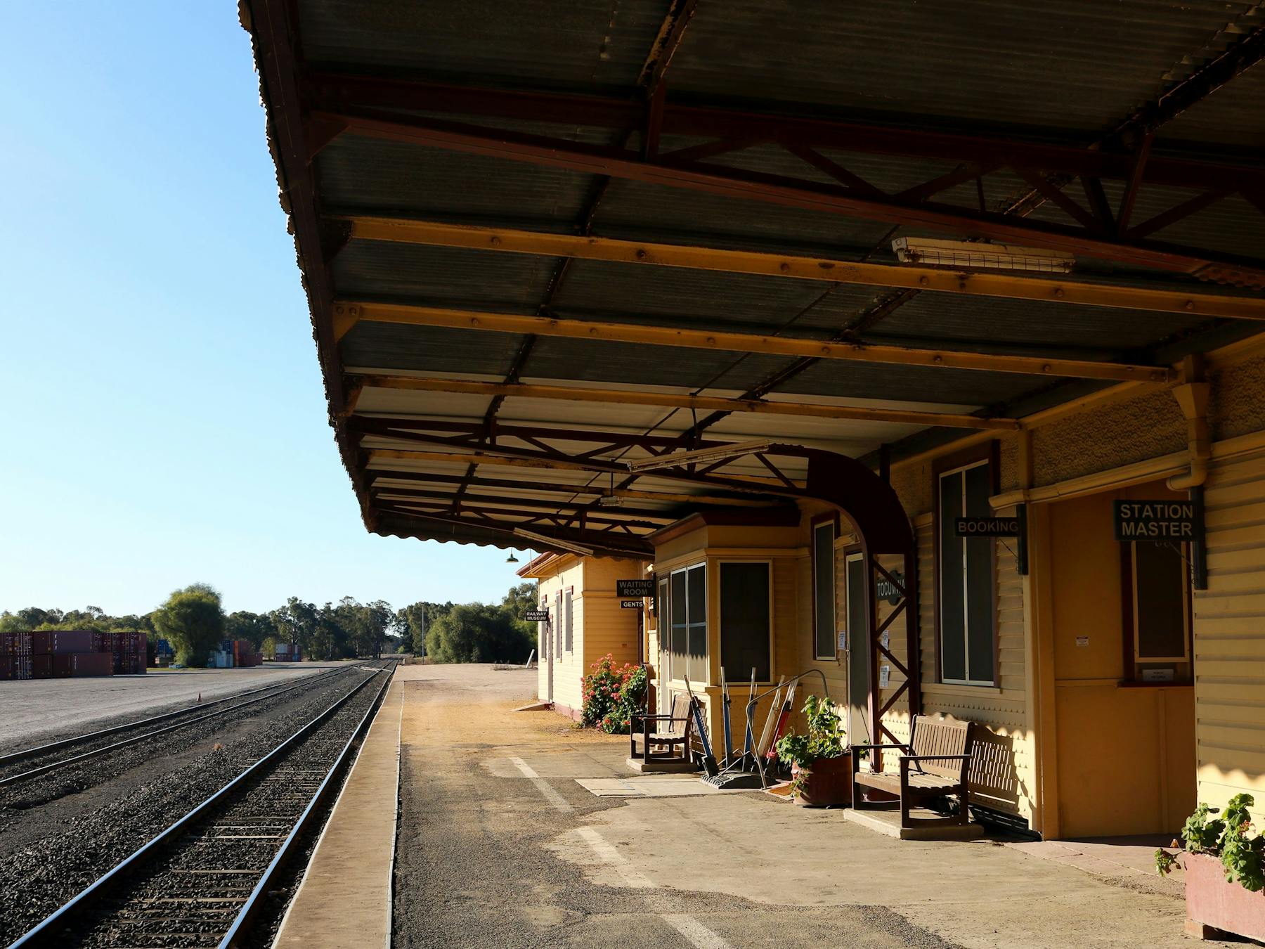 Railway Station platform, with railway track on the left and verandah-covered station on the right