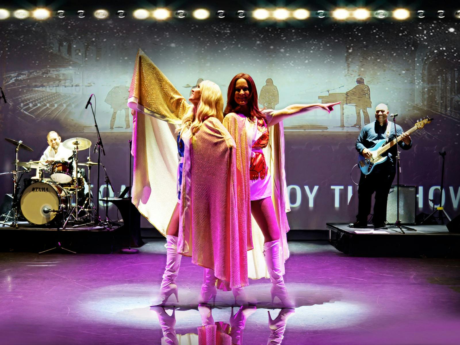 Two women standing back to back in 70s era clothing - white boots and gold capes Two women standing back to back in 70s era clothing - white boots and gold capes