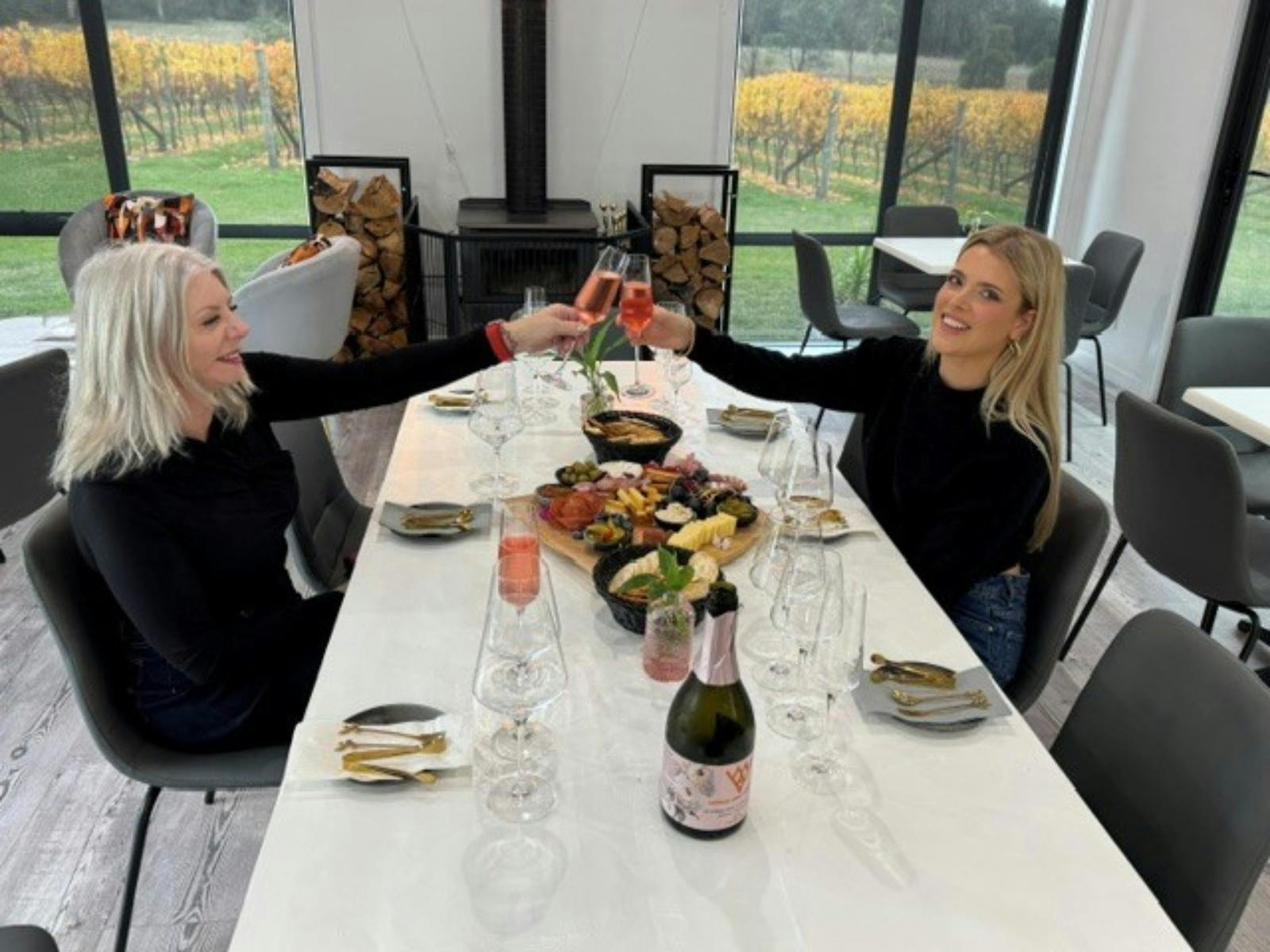 Two ladies with wine, cheersing over a platter of Tasmanian produce in a cellar door.