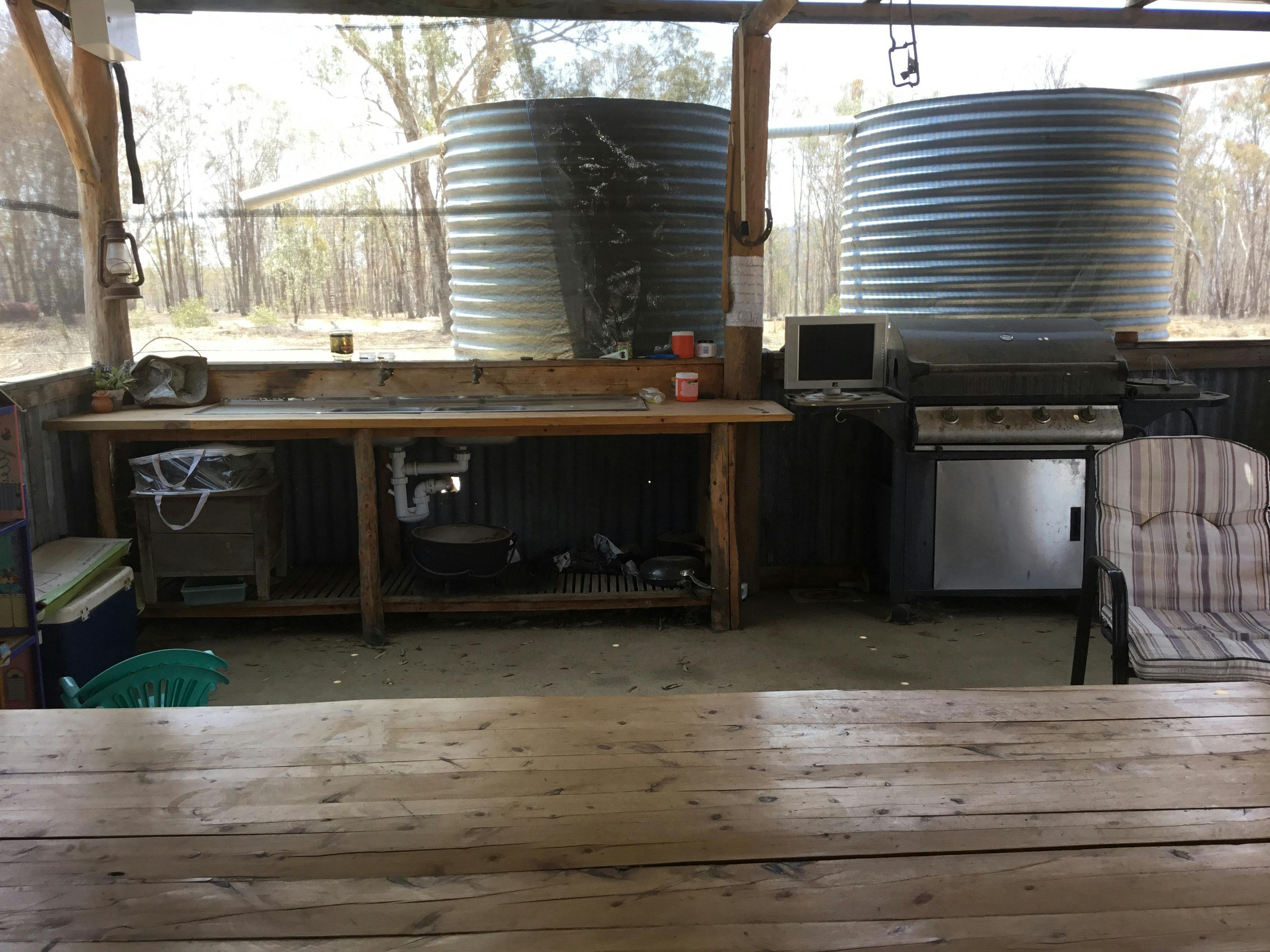 Rustic Kitchen with two wooden benches, sink and BBQ with two water tanks behind the BBQ.