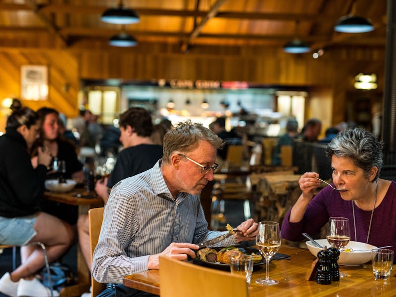 Couple eating a meal in Kauri Bistro with other patrons & Cape Grim Grill visible in background