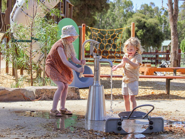 2 children play at water pump at playground