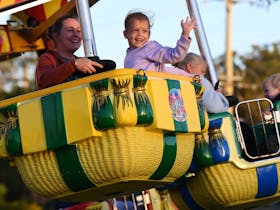 Child smiling and waving on a ride at the Beenleigh Cane Festival