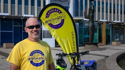 Man in yellow and purple branded t-shirt standing in front of yellow flag