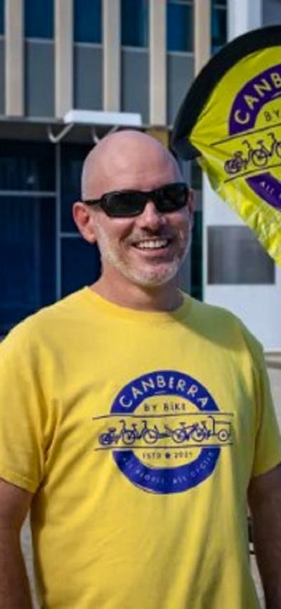 Man in yellow and purple branded t-shirt standing in front of yellow flag