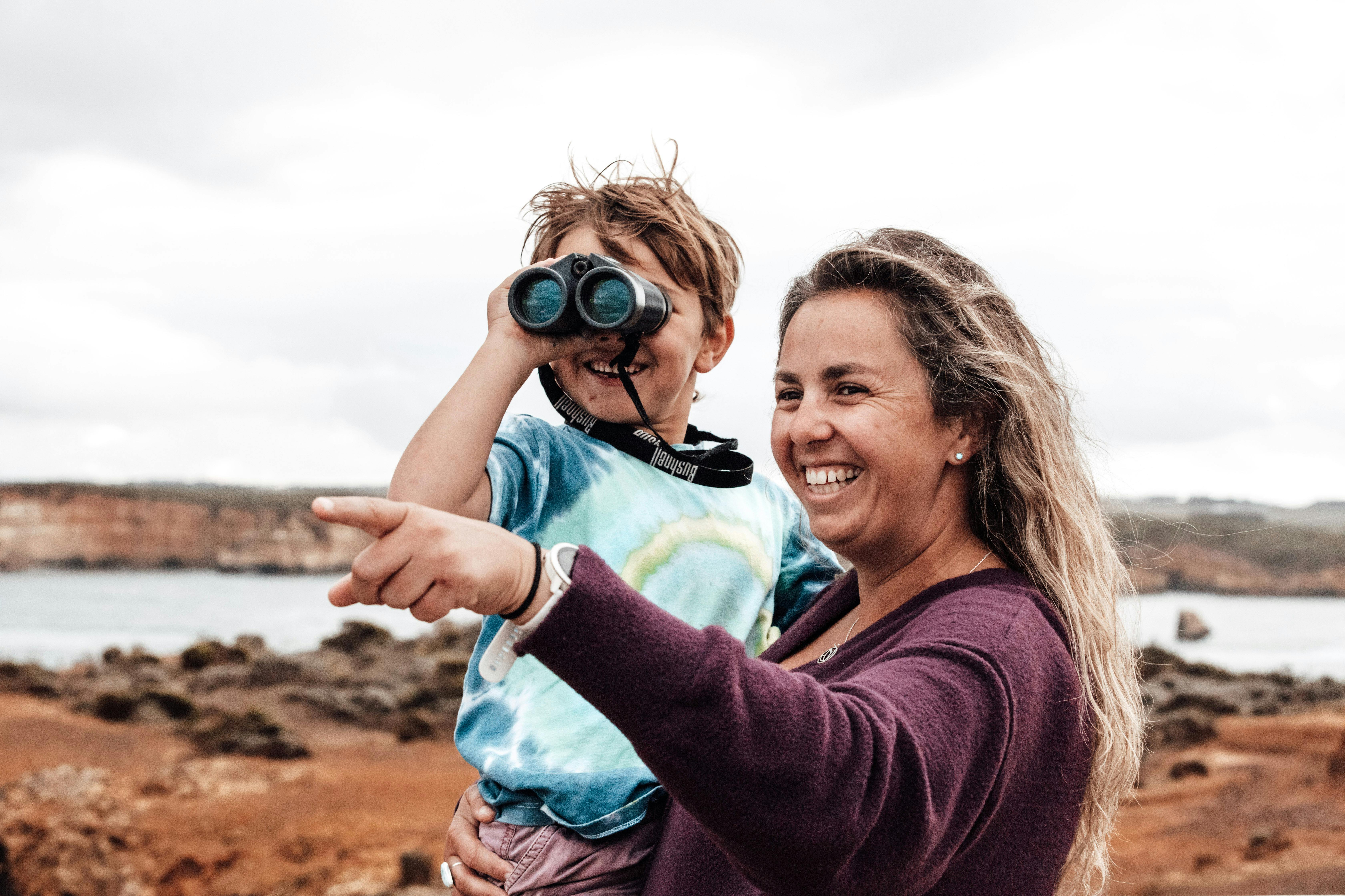 Mum holding her son as she points while he is looking through binoculars
