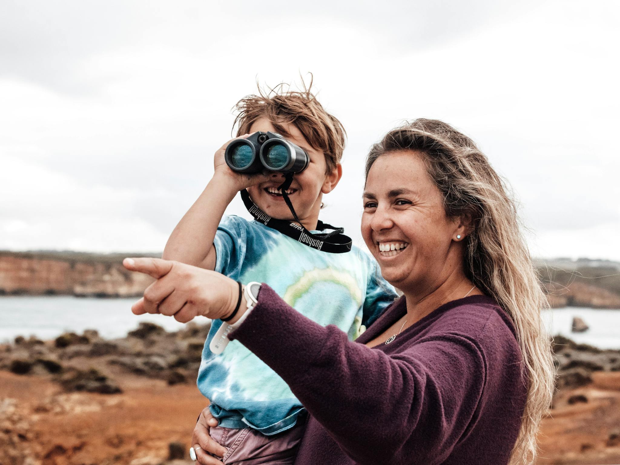Mum holding her son as she points while he is looking through binoculars