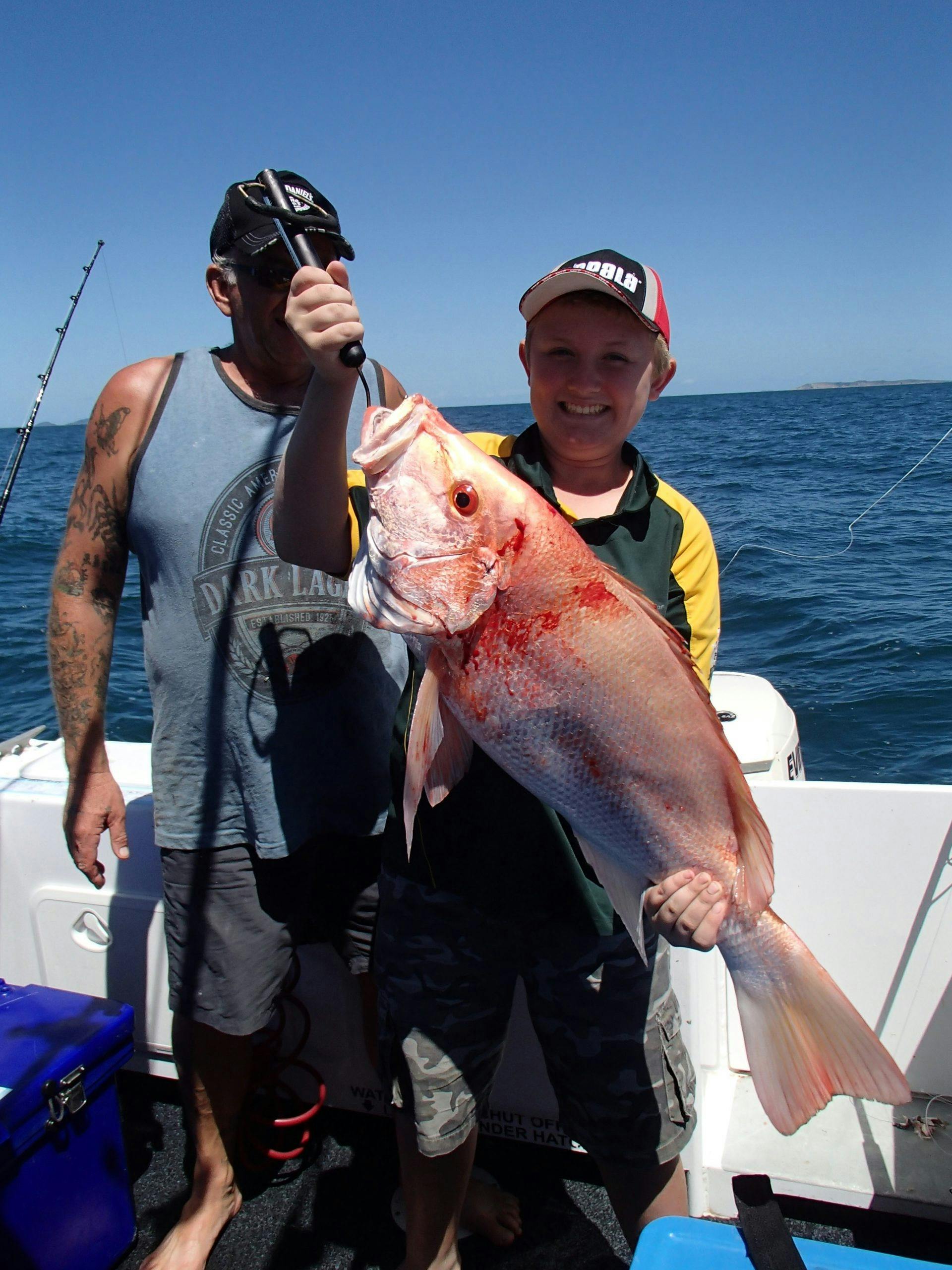 Young boy holding a fish that he has caught whilst on tour, another angler standing behind him.
