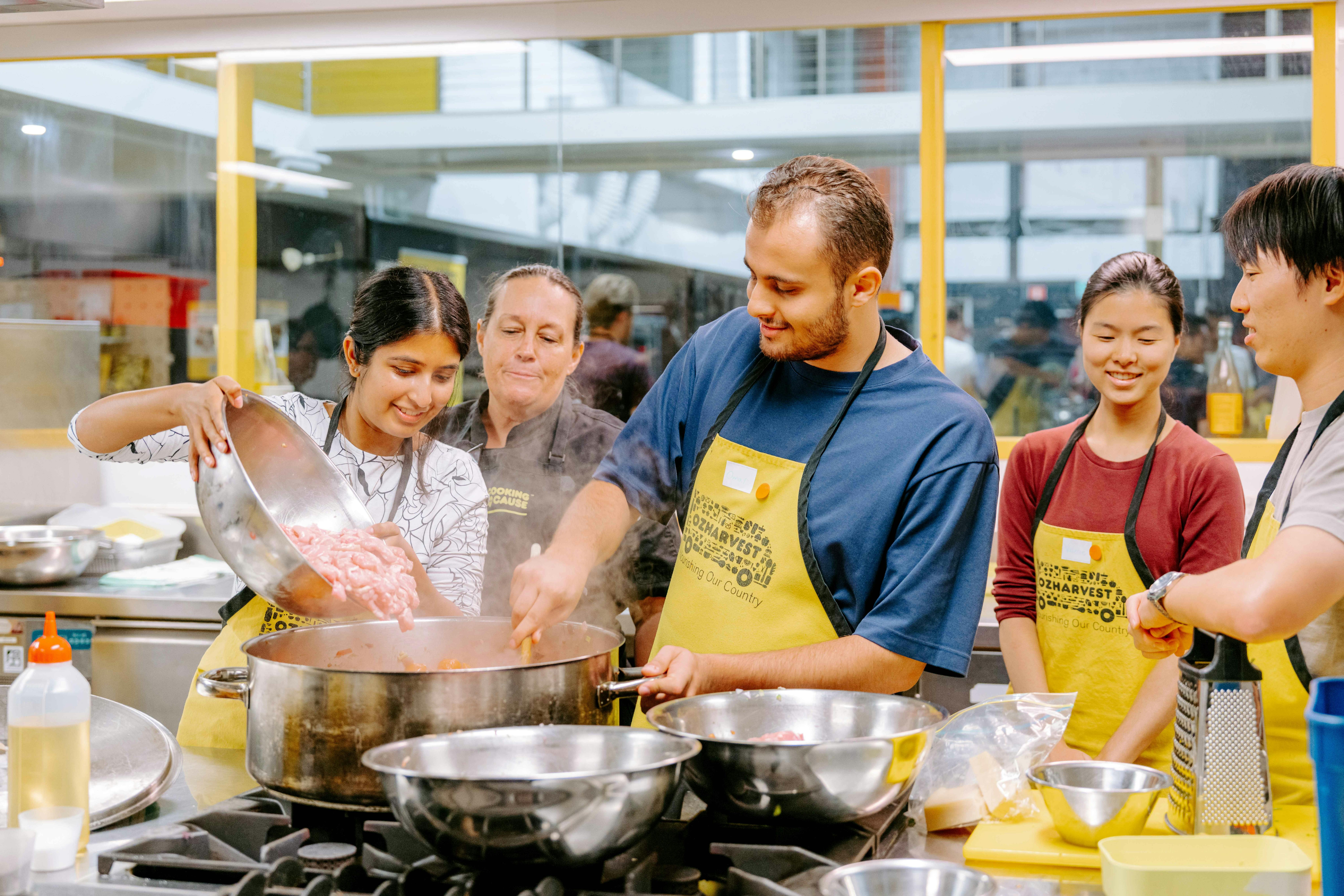 Participants at an OzHarvest Cooking for a Cause cooking class gathered around a stove, adding mince