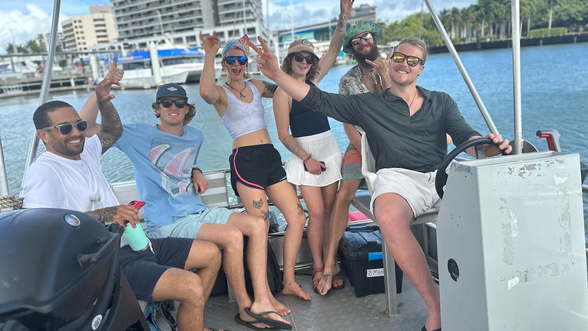 Smiling group of 6 friends waving on a Cairns Boat Hire Pontoon in Tropical North Queensland