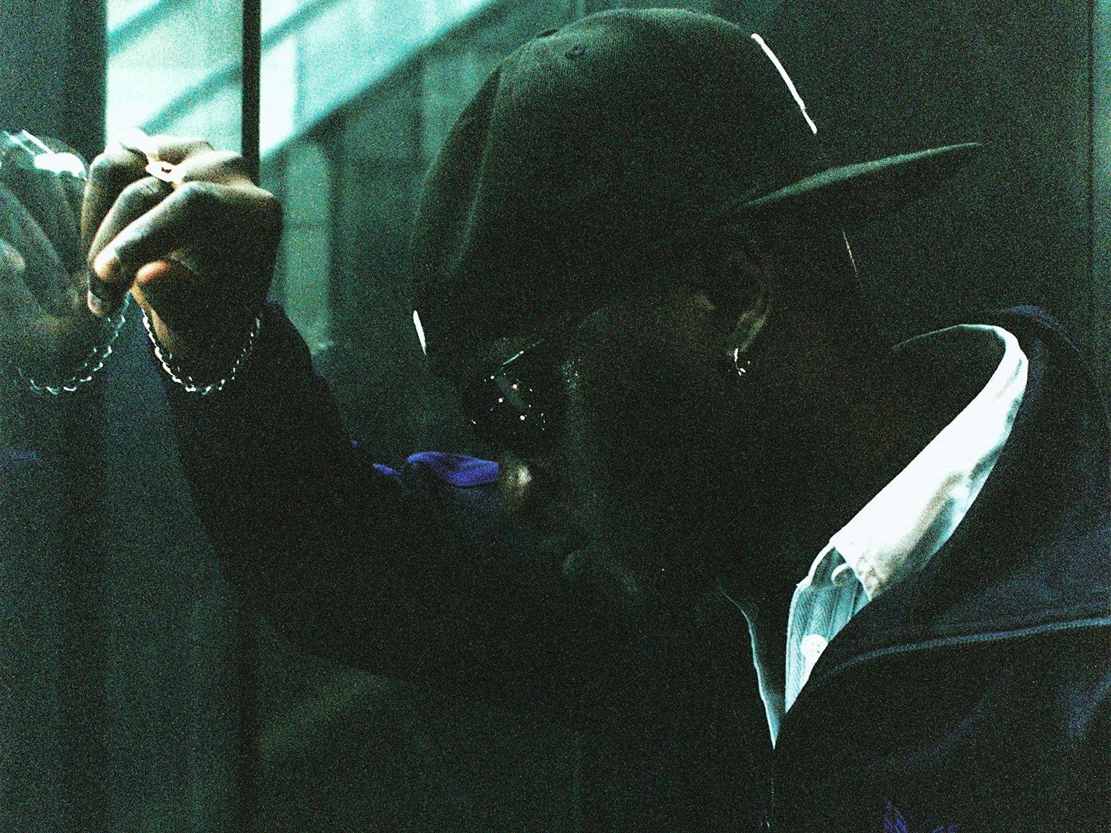 A person in a dark, reflective space looks down while resting their head on their hand against wall