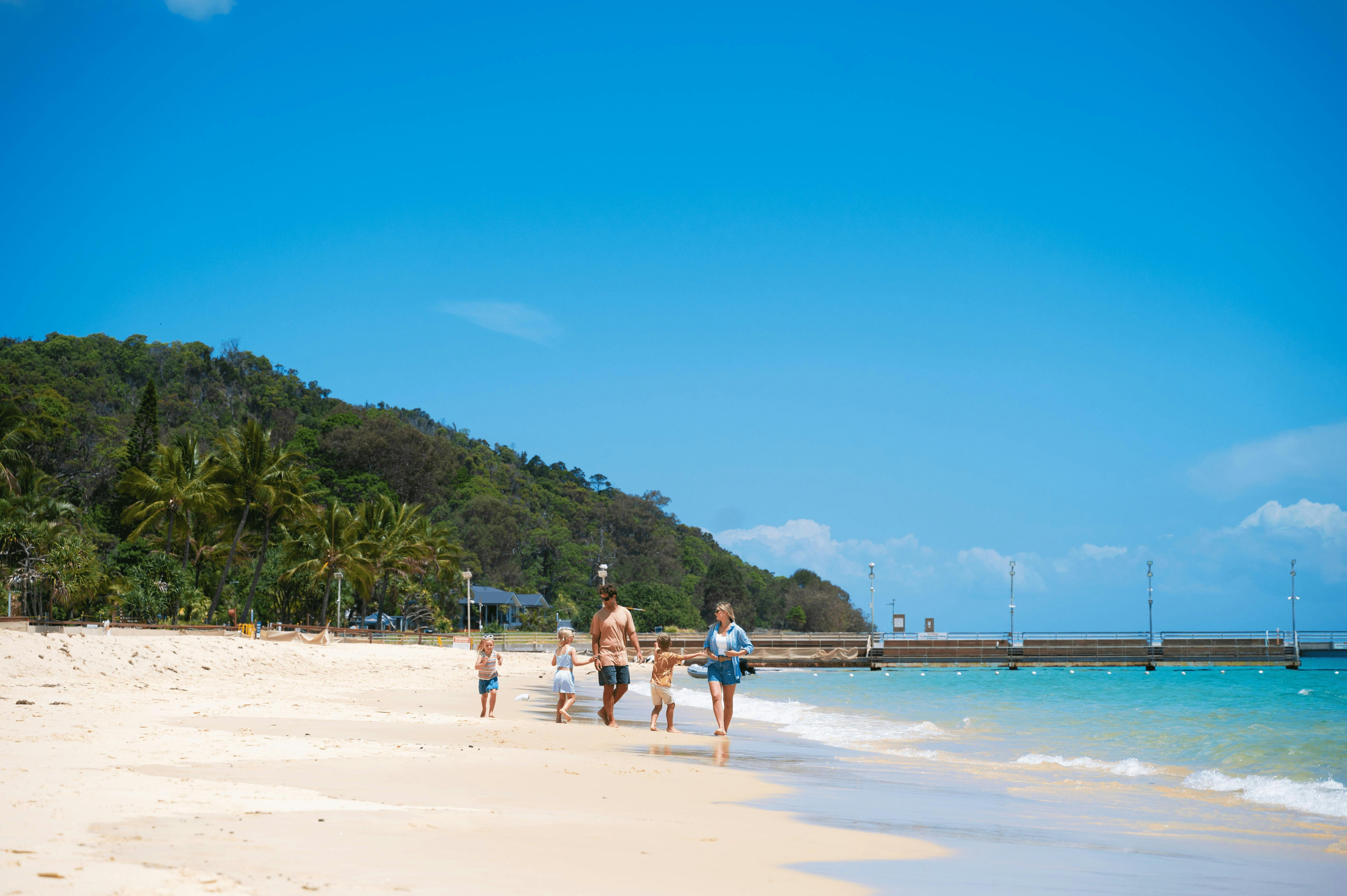 Family walking along the Tangalooma beach with Moreton Island greenery in the background