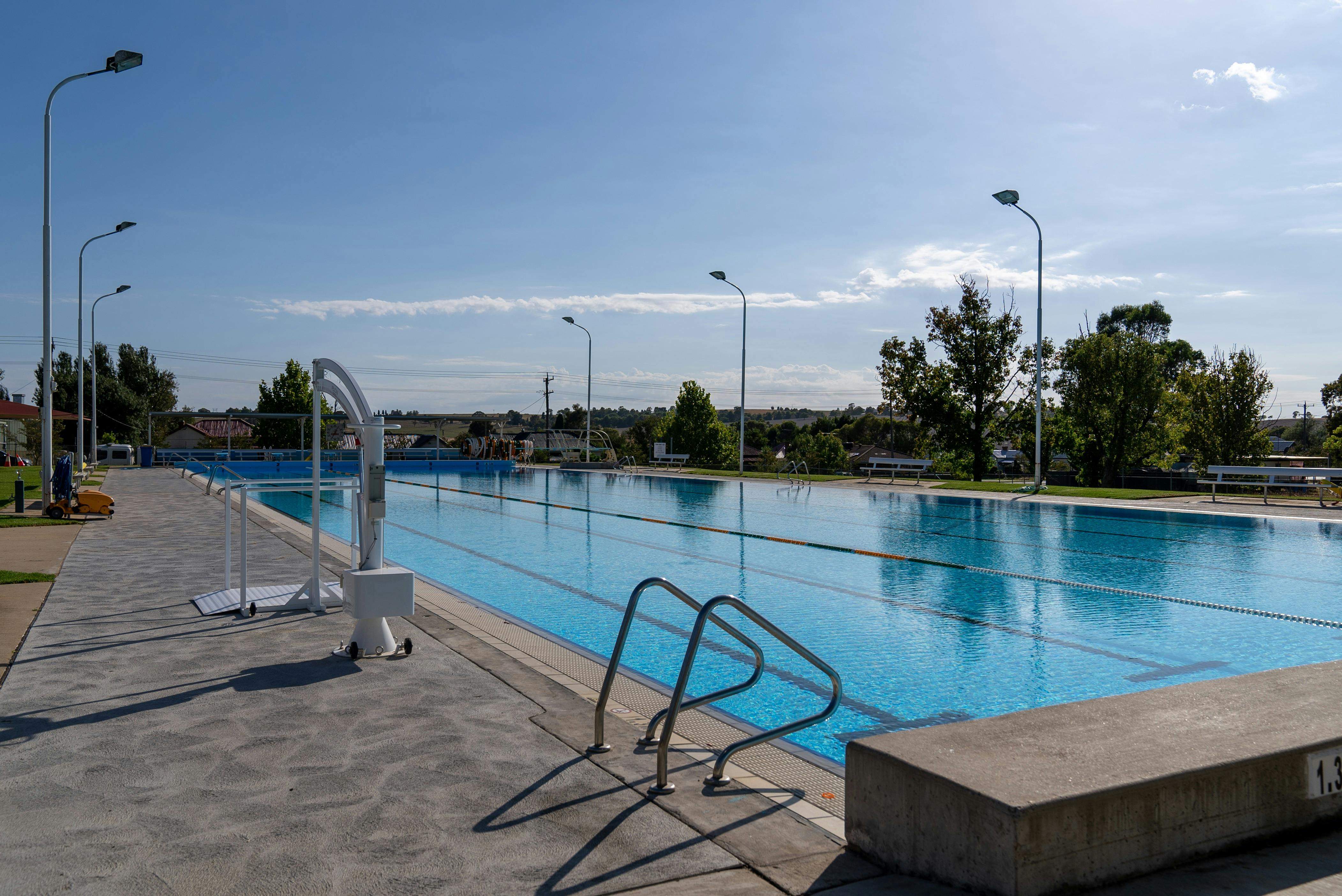 Harden Pool in the sunlight, seen from by the edge, with steps and chair seat. Trees in background.