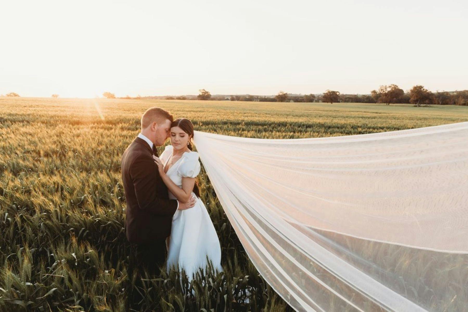 Bride and groom embracing in a field at sunset.