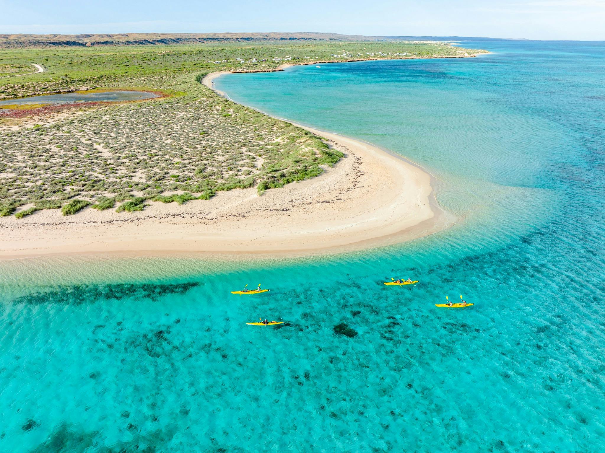 An aerial view of yellow kayaks on turquoise water, with a white sandy beach in the background.