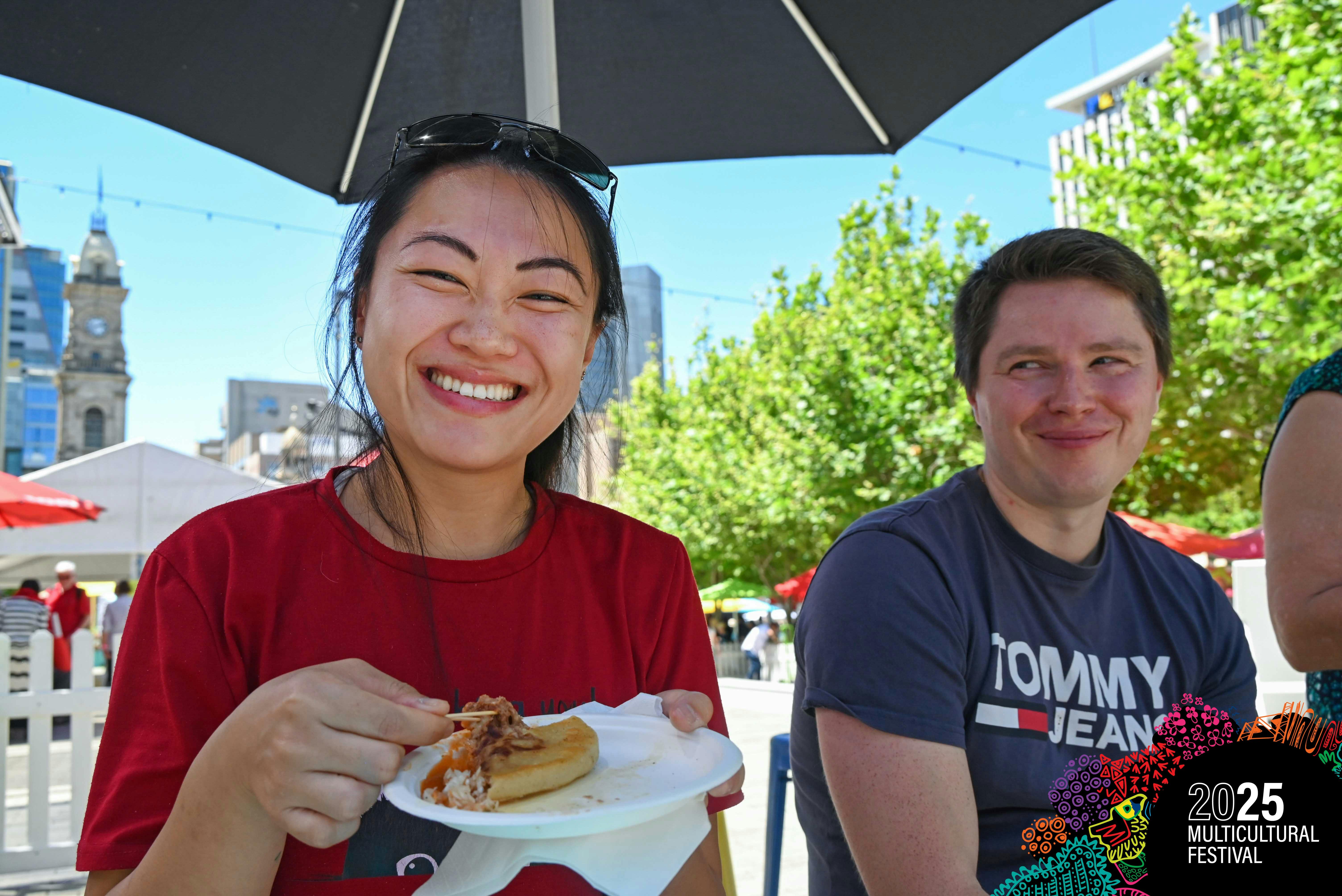 A man and a woman are smiling at the camera while trying papusas