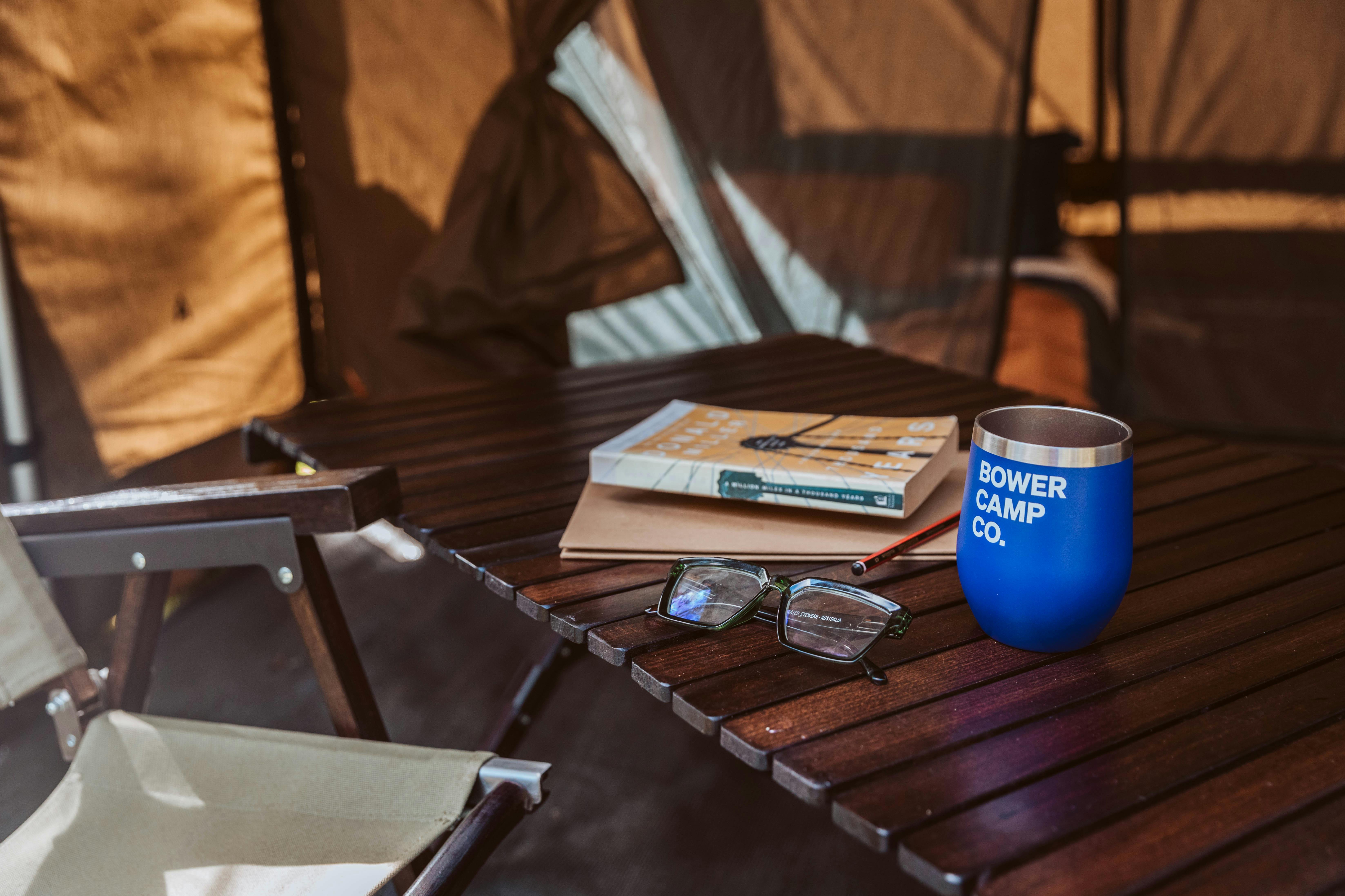 Interior of tent with table, chair, books, glasses and a Bower Camp Co. mug.