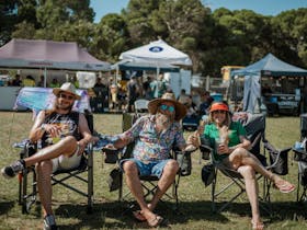 Two men and a woman chilling out in their deck chairs as they watch the live music on stage at COFU