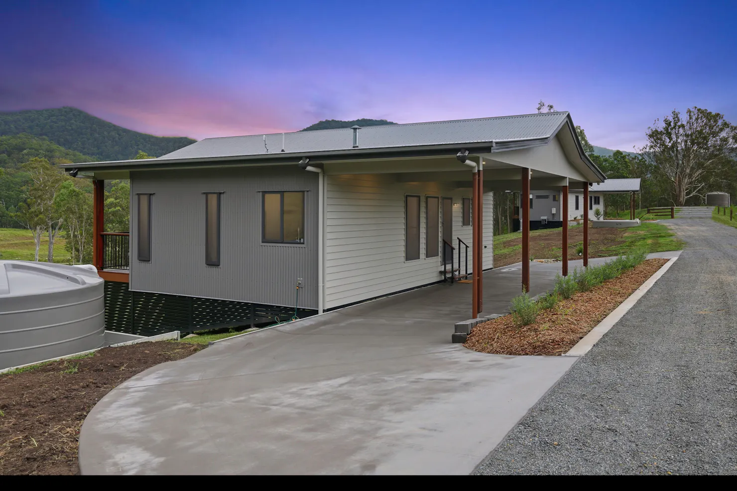 Modern lodge exterior with driveway, water tank, and hills in the background