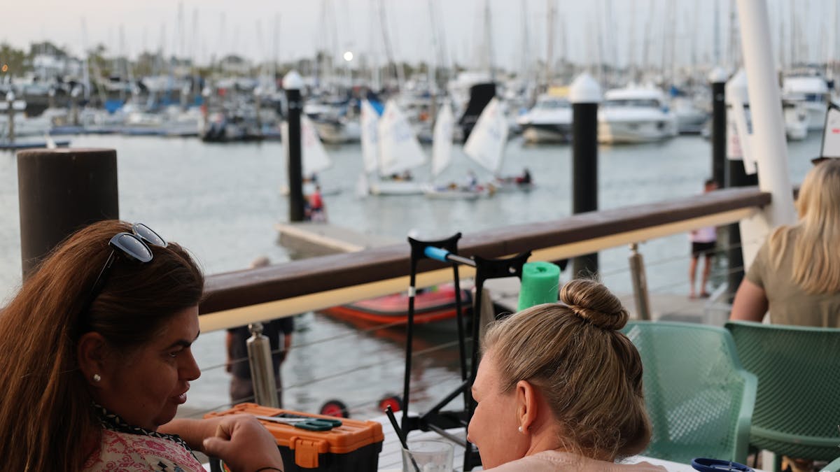 People sitting on a boardwalk watching boats go by