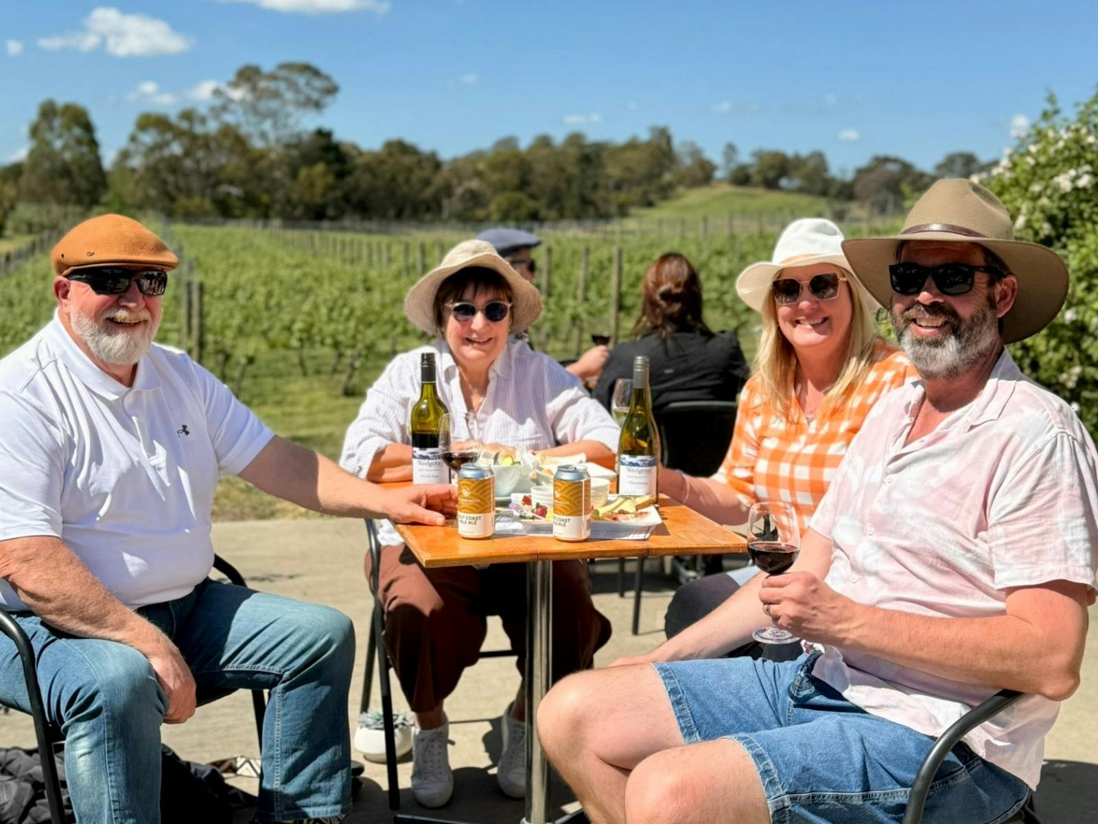 Group of 4 people enjoying wine at a table with a vineyard in the background