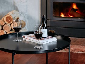 Bottle of red wine with two glasses on coffee table with fireplace in background