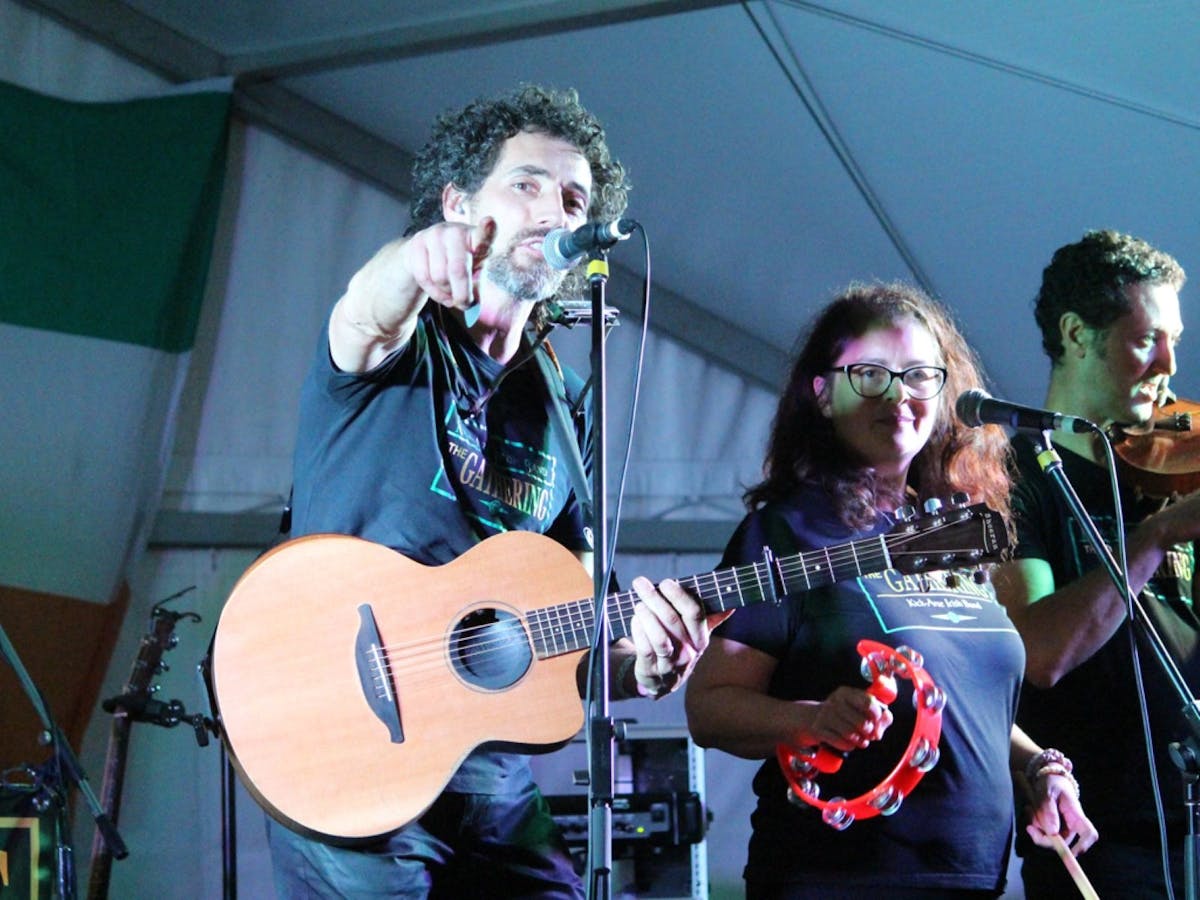 A guitarist points at the camera, with a percussionist looking on and fiddle player in background