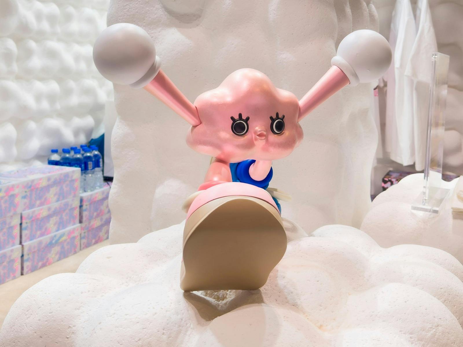 Pink cartoon character with large eyes and extended ears sits on fluffy white clouds