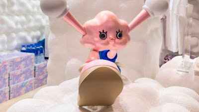 Pink cartoon character with large eyes and extended ears sits on fluffy white clouds