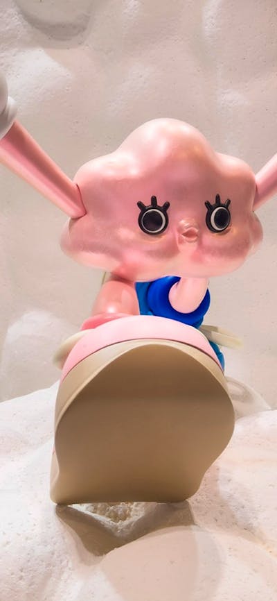 Pink cartoon character with large eyes and extended ears sits on fluffy white clouds