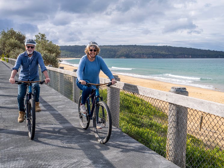 Two guests cycle along the boardwalk next to Aslings Beach Eden