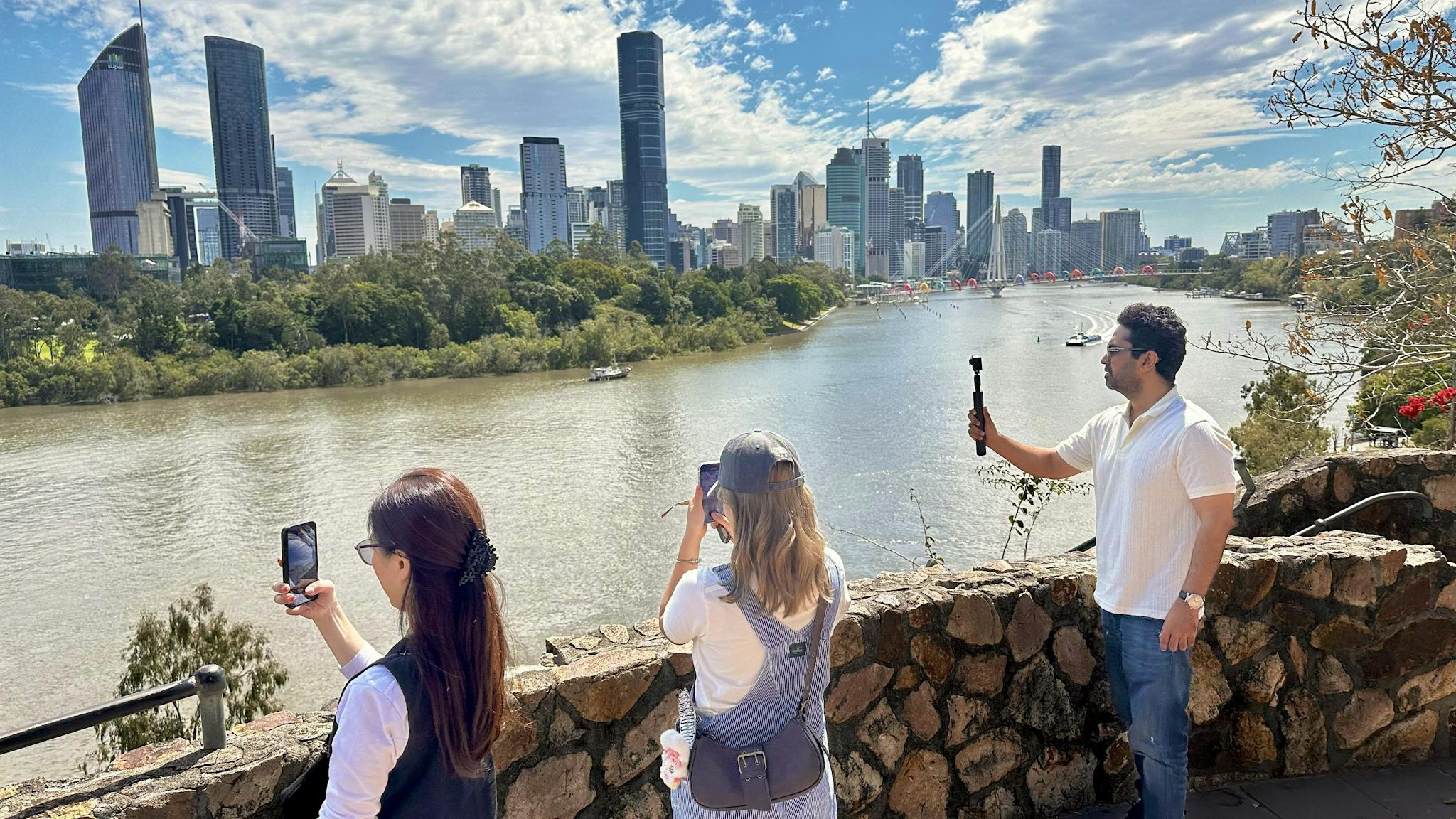 Three people taking photos of river. City skyline in the background. Three people taking photos of river. City skyline in the background.