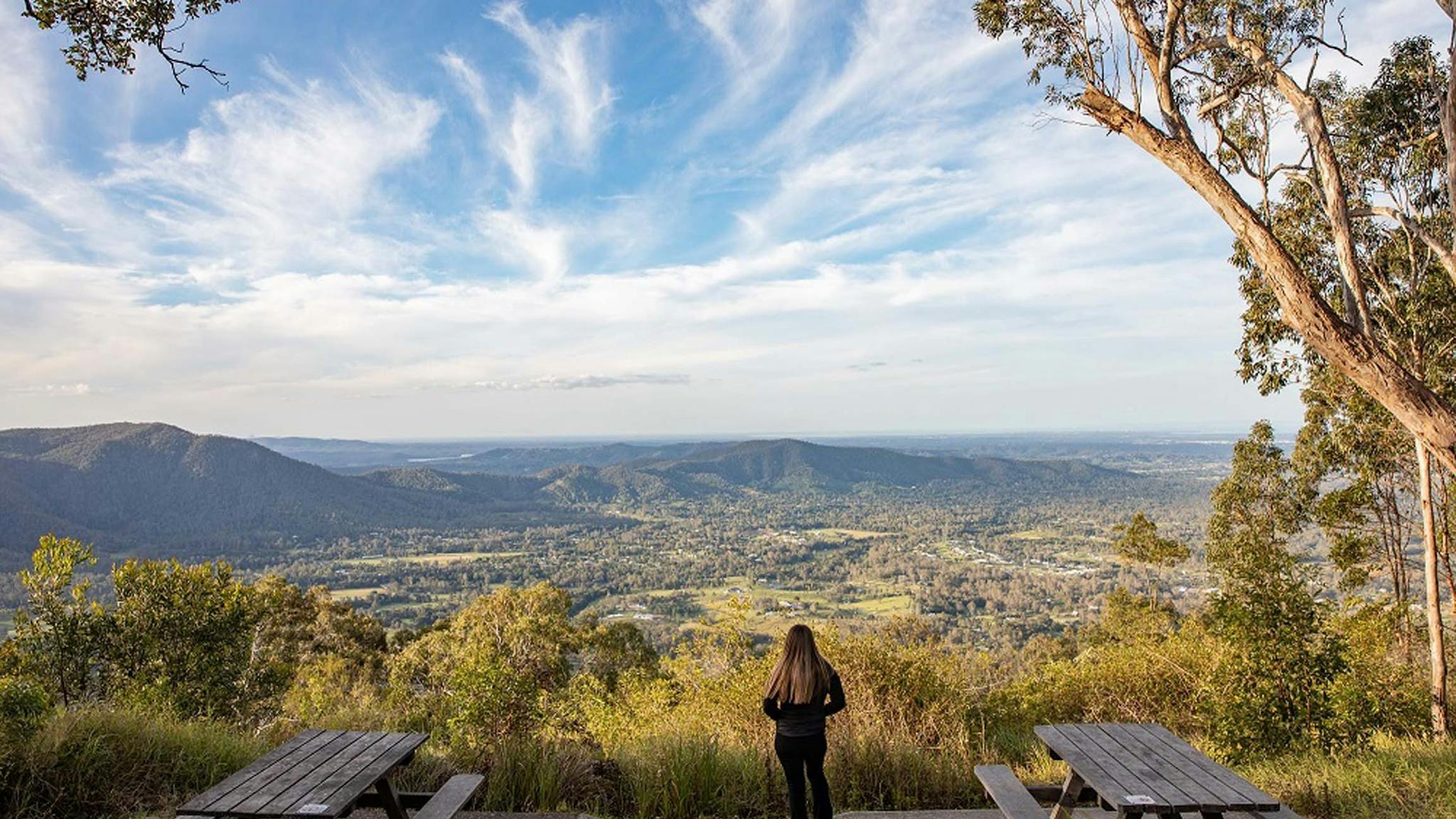 Woman standing between two picnic tables looking out over mountains