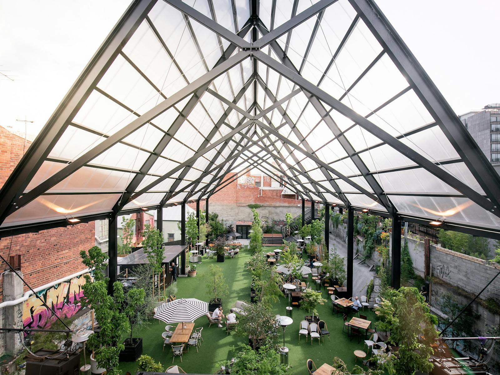 The 18 metre tall Cathedral black frame shelters the lawn space with tables and plants beneath