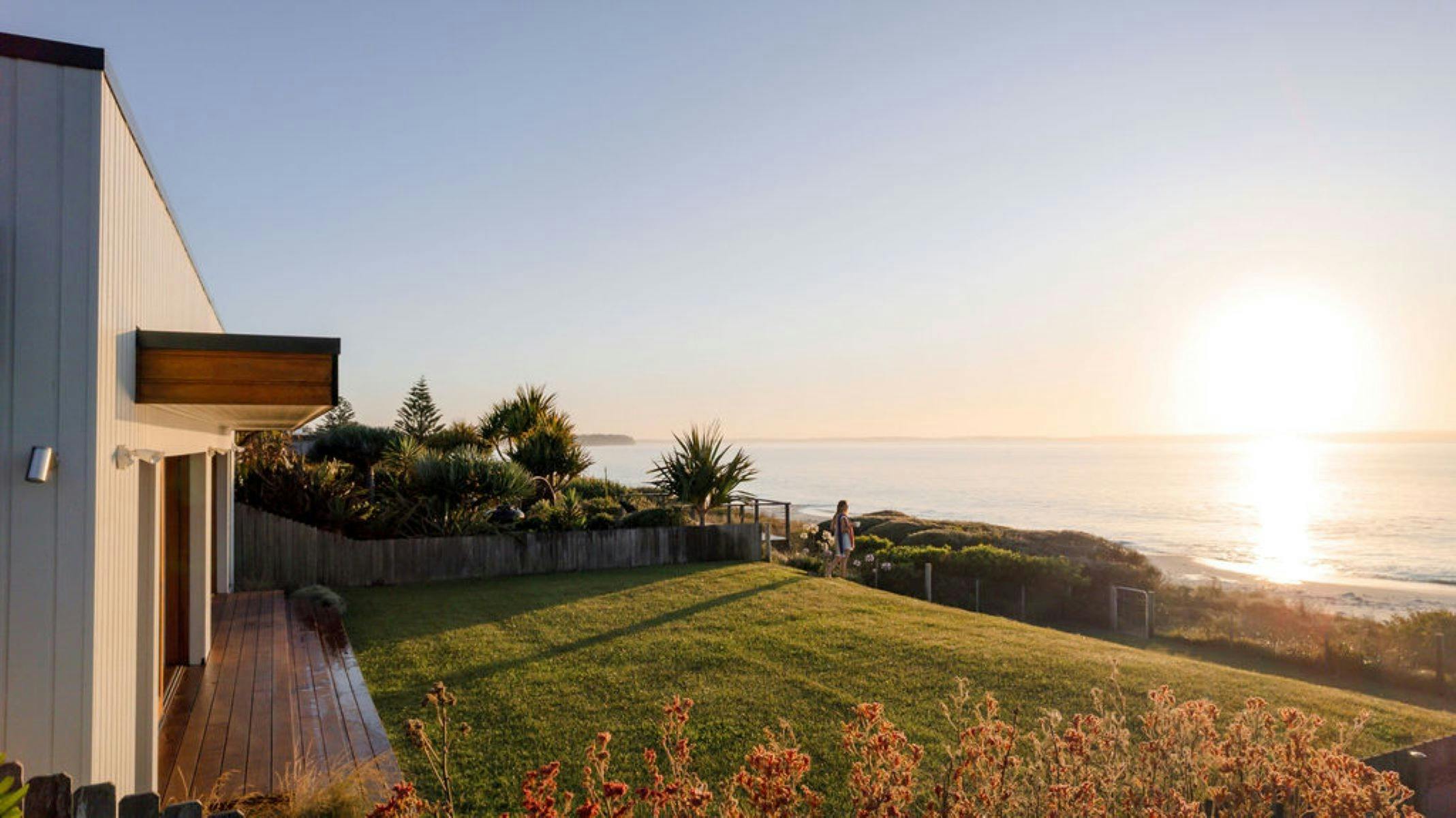 Image of back yard of property rolling onto the beach front loctation. Lady enjoying coffee on left.