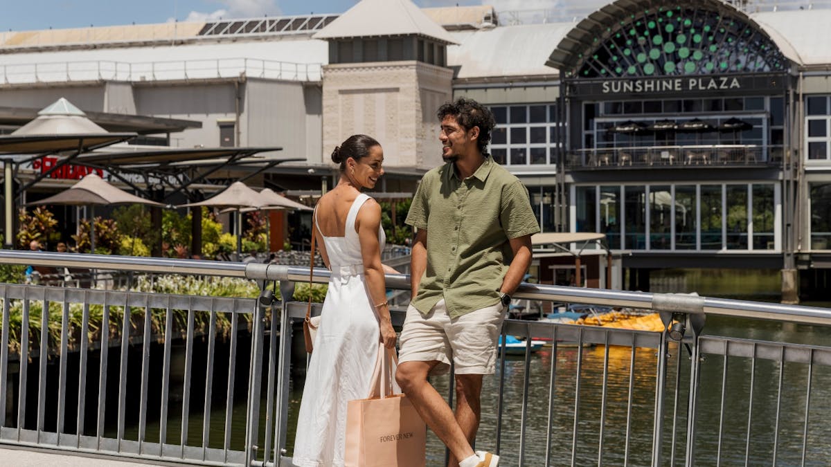 Couple standing outside on bridge in front of Sunshine Plaza logo