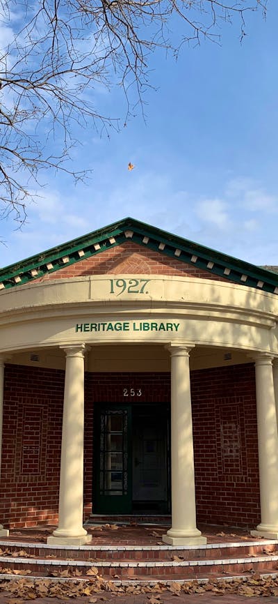 Image of 1920's red brick building with cream portico, green arched windows, and two flag poles.