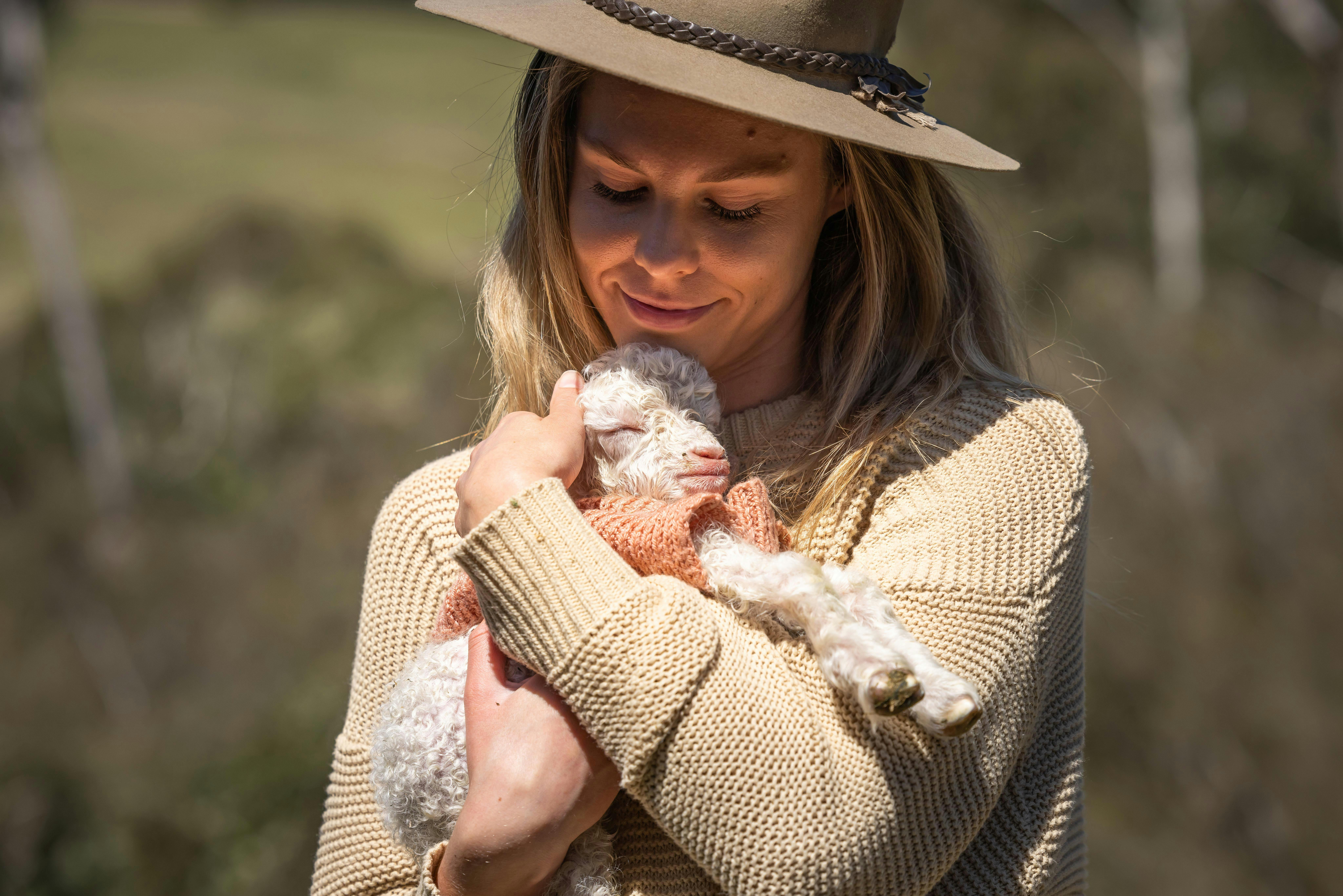農場で子ヤギの出産シーズン中に、ピンクのジャンパーを着た子ヤギを抱いている女性