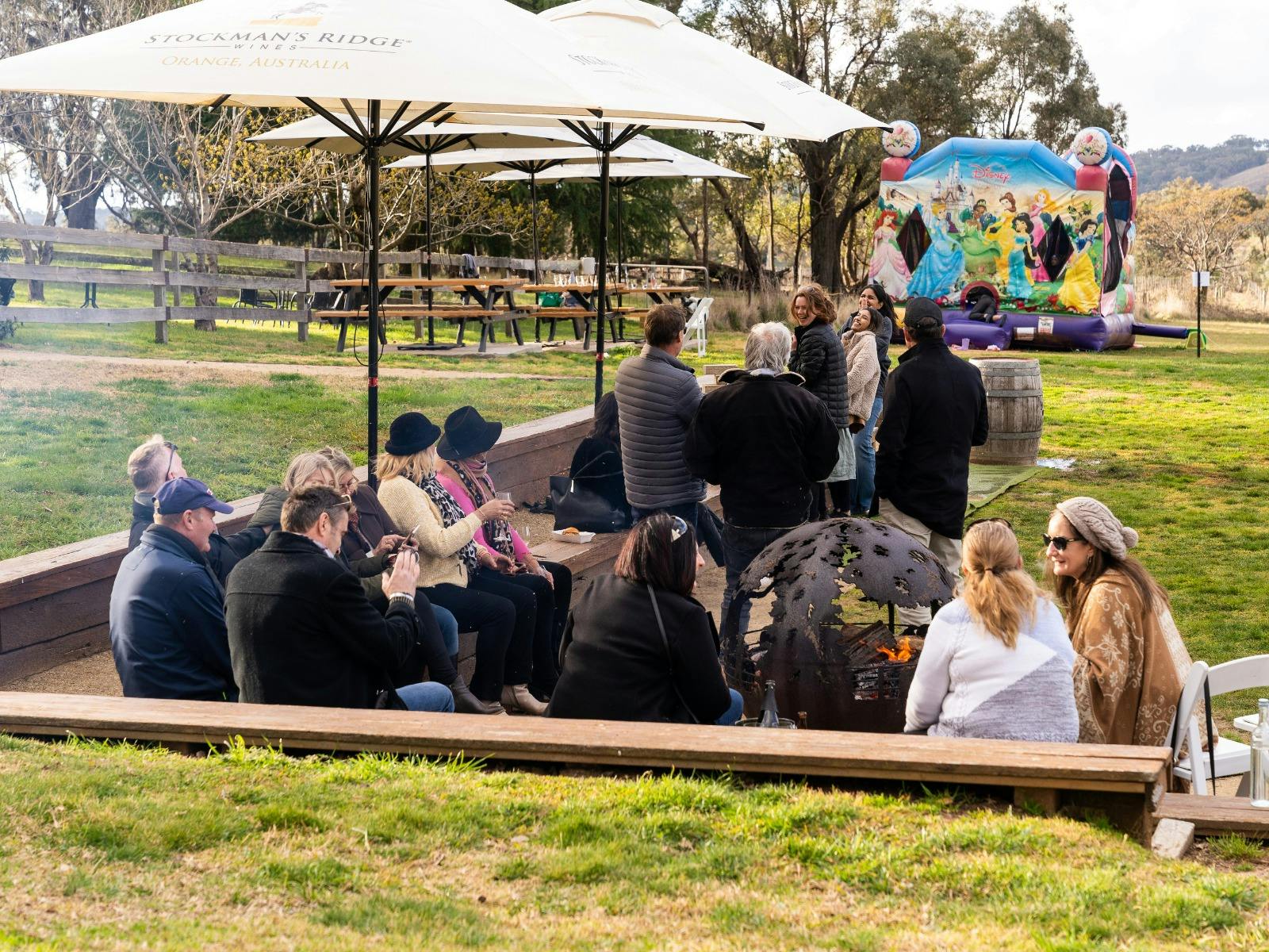 friends around firepit with forest and jumping castle in background at Stockmans Ridge Wines