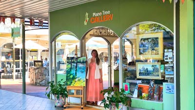 Gallery street frontage with displayed artworks hanging in window and on easel and co-owner standing