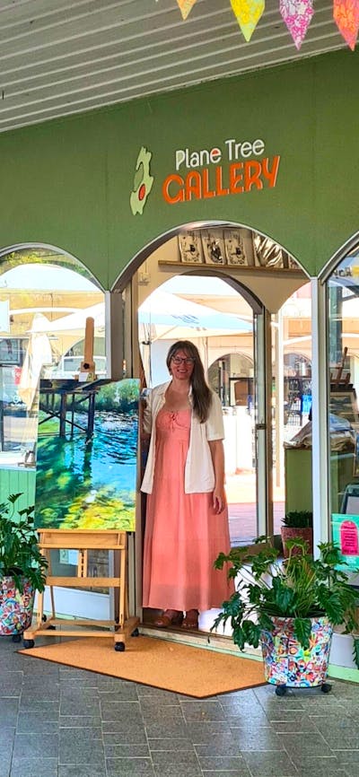 Gallery street frontage with displayed artworks hanging in window and on easel and co-owner standing