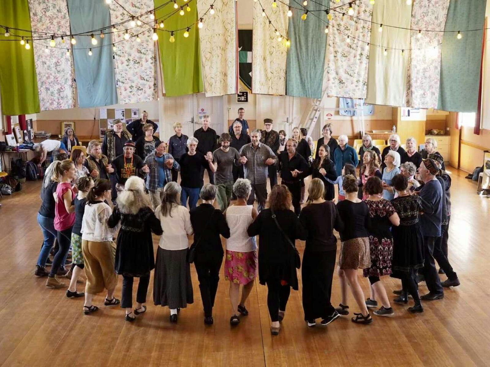 Large group of people standing in a circle linking arms nad singing