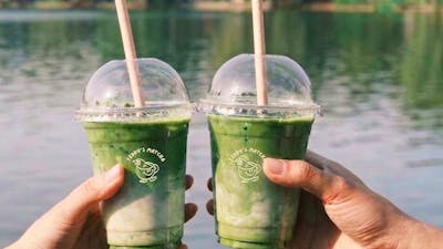 two matcha cups being held in two different hands doing a cheers in front of a lake background