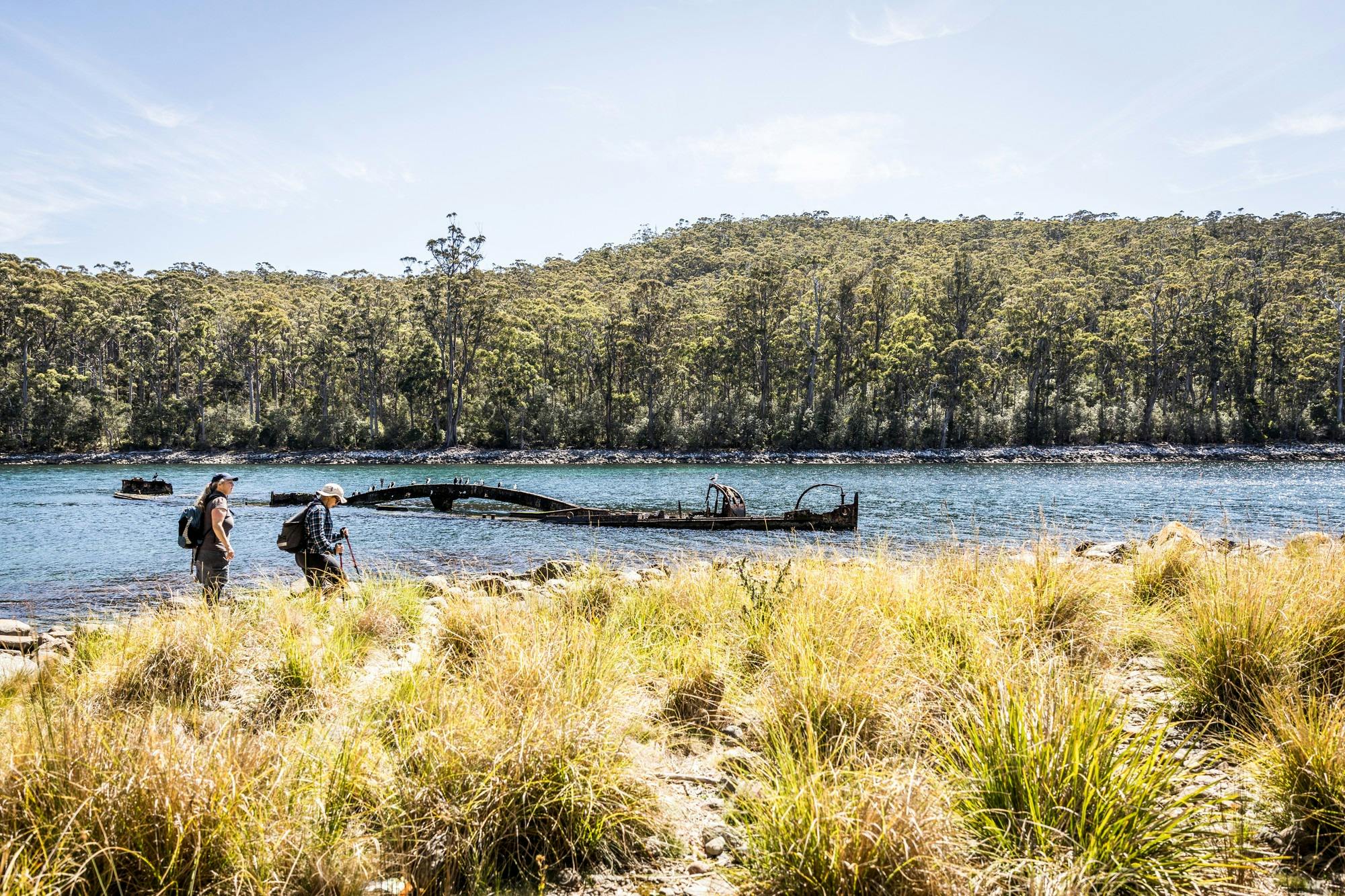an image of views across canoe bay with walkers viewing the remains of a partially submerged barge