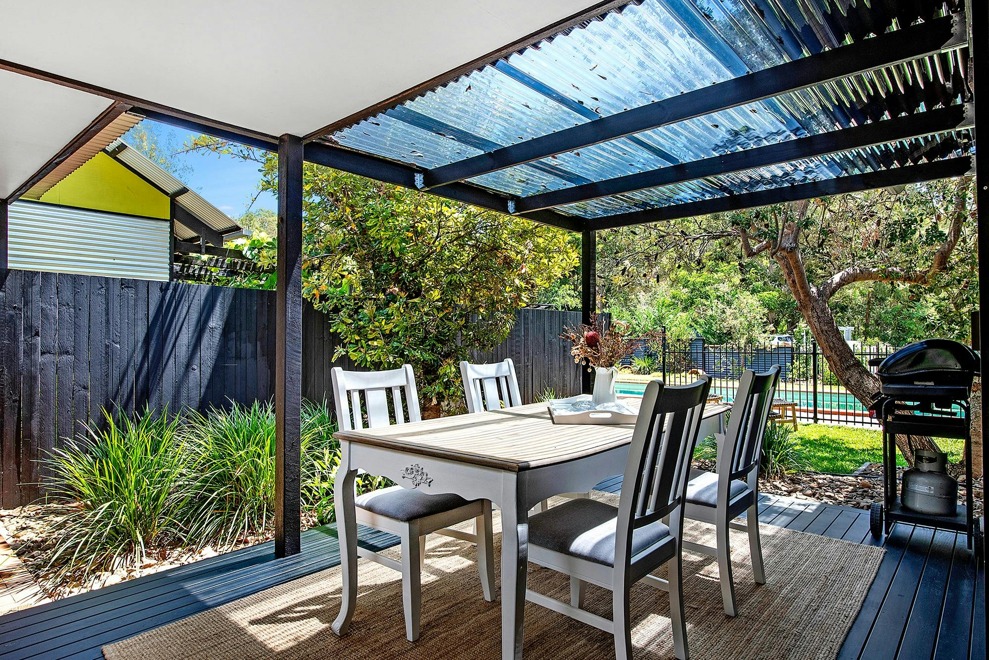 Covered alfresco BBQ deck overlooks the fire pit and swimming pool