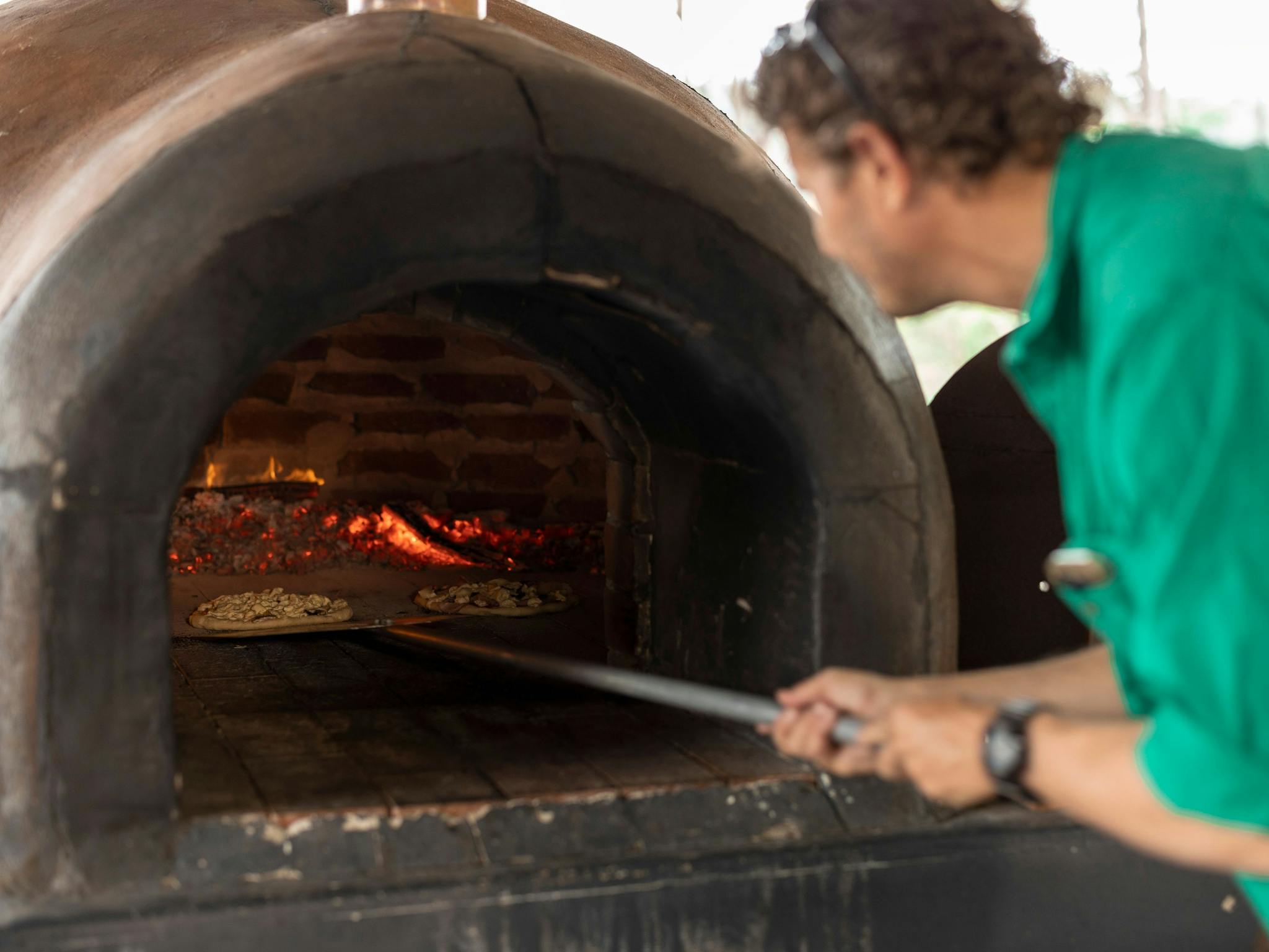 Man placing pizza in a wood fired oven