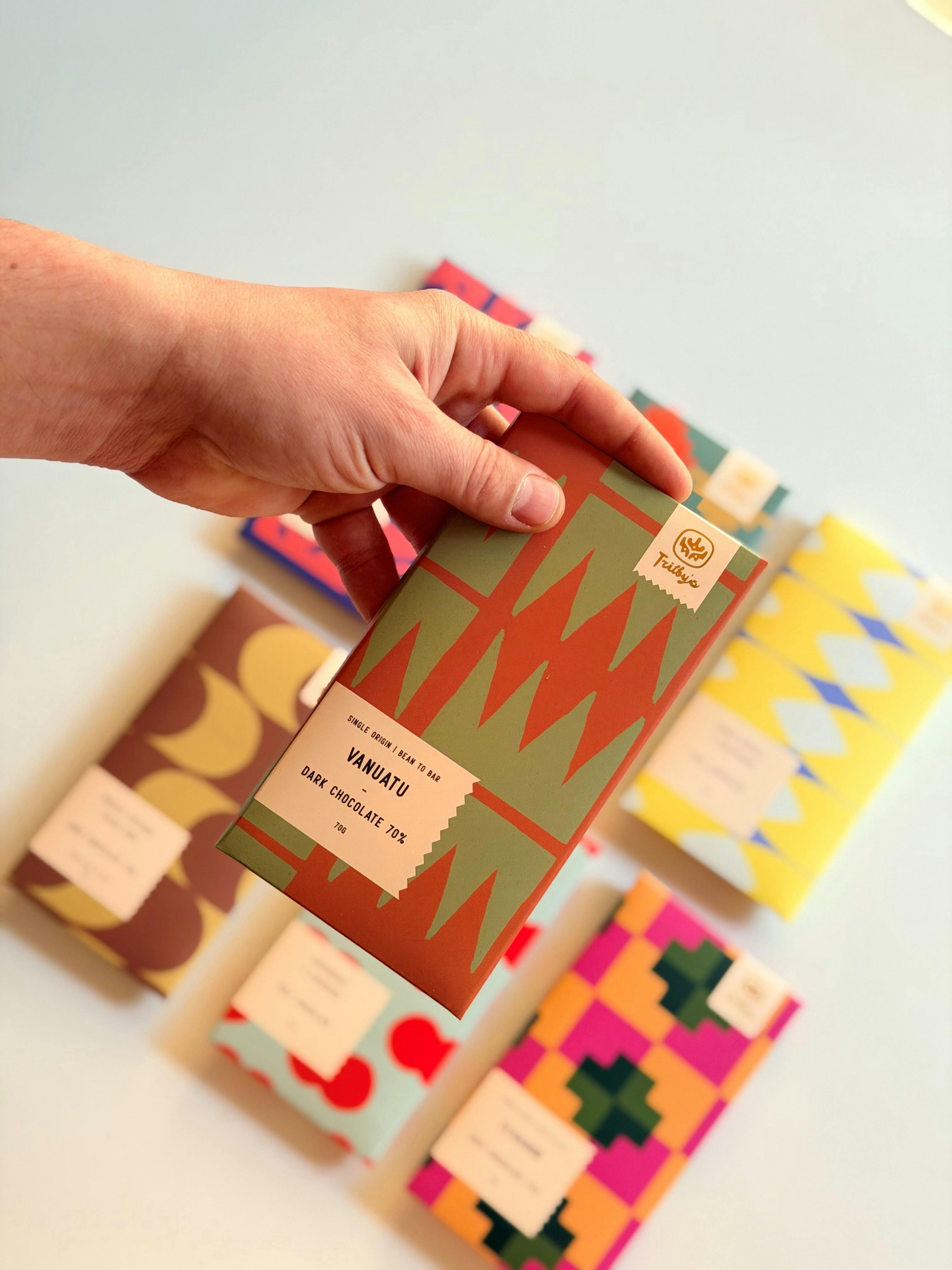 Hand holding a Vanuatu 70% Dark Trilby’s chocolate bar with others blurred behind.