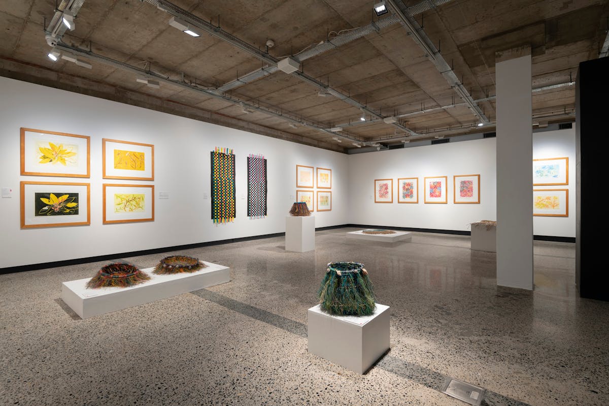 Gallery with white walls and a polished concrete floor. Artworks are monoprints and woven baskets.